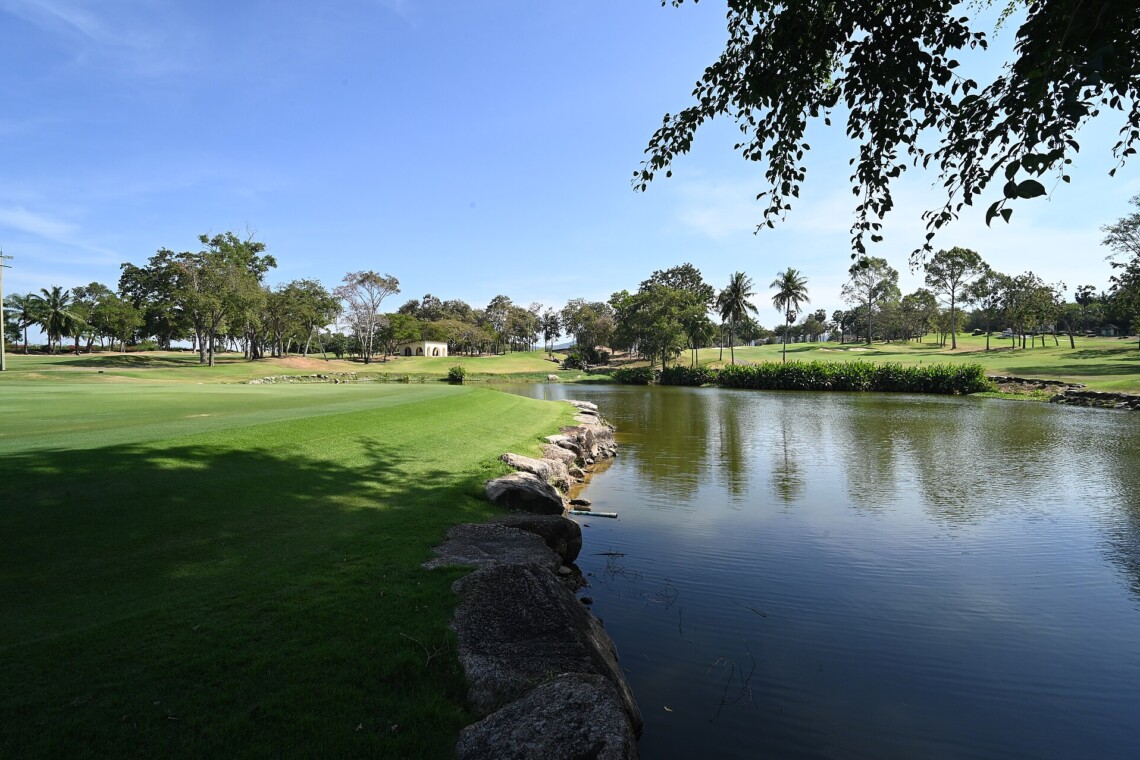 Sunlit golf fairway beside a calm water hazard lined with palm trees
