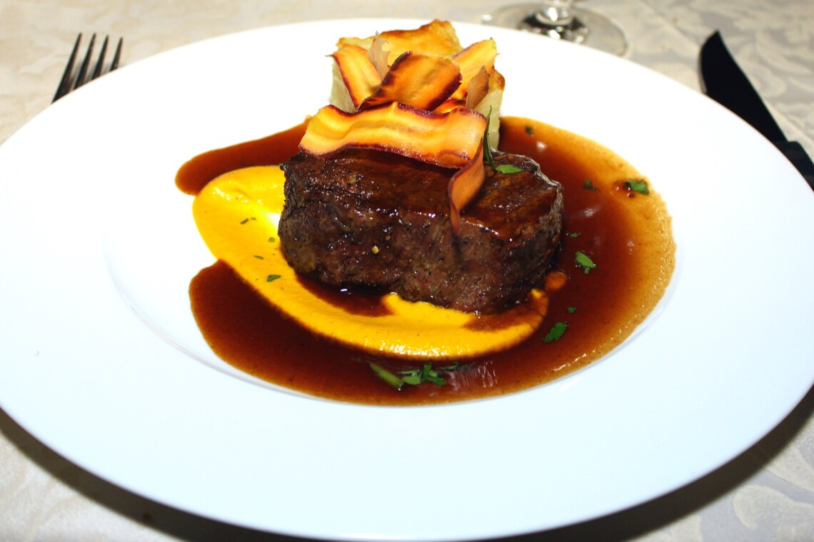 Grilled fillet steak served with sauce and vegetable garnish on a white plate