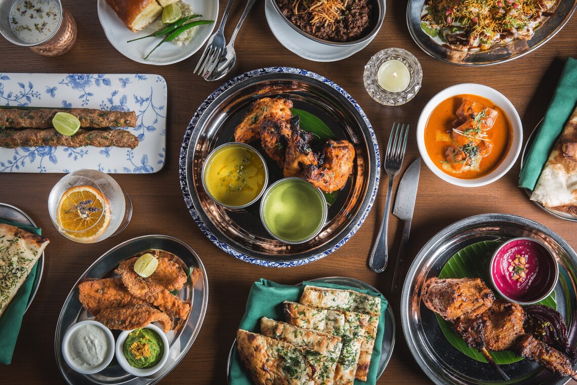 Indian restaurant table spread with tandoori chicken, kebabs, naan bread and curries