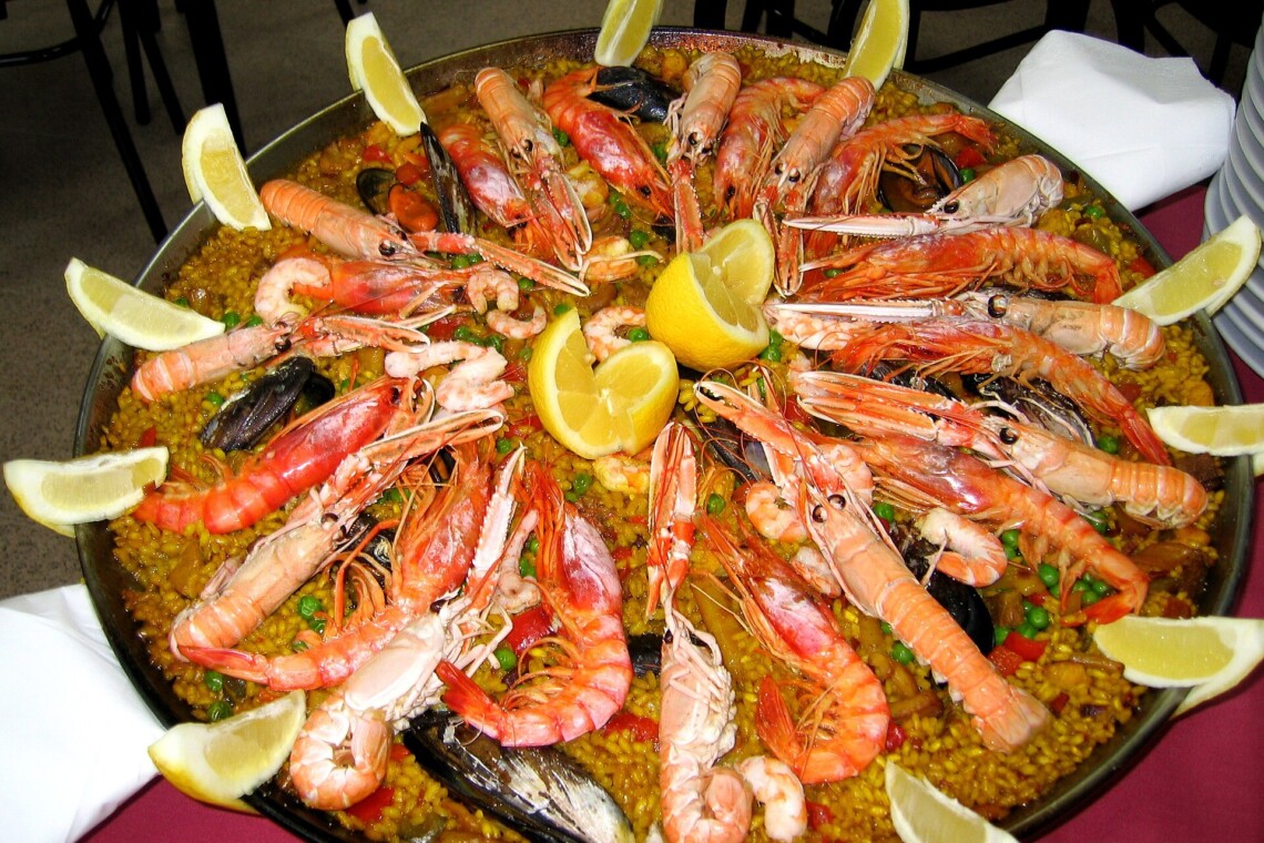 Seafood paella in a wide pan with langoustines, prawns, mussels and lemon wedges