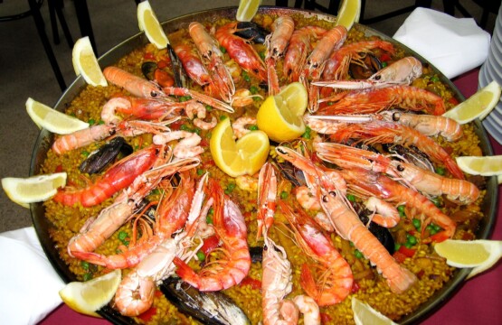 Seafood paella in a wide pan with langoustines, prawns, mussels and lemon wedges