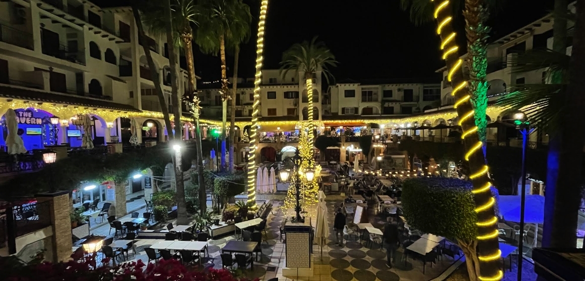 Villamartin Plaza on a summer night with lit palm trees and busy restaurant terraces